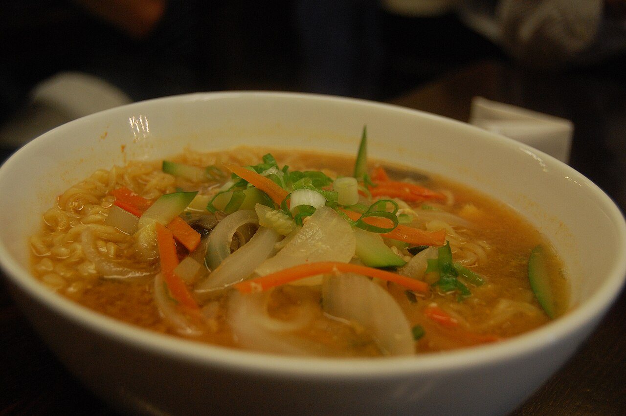 A bowl of Korean instant noodles in red broth with egg and spring onion