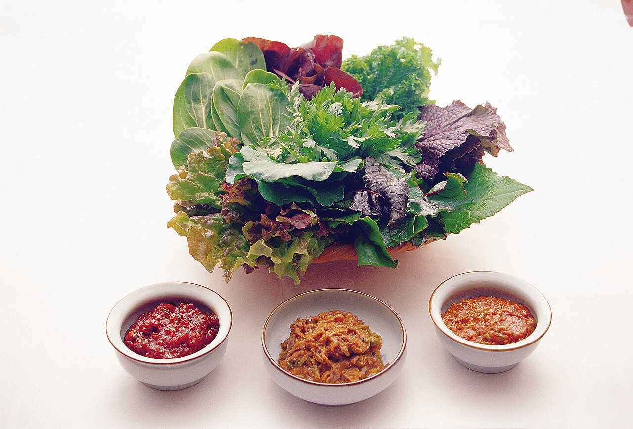 A pile of lettuce and leaves for wraps with three small bowls of paste